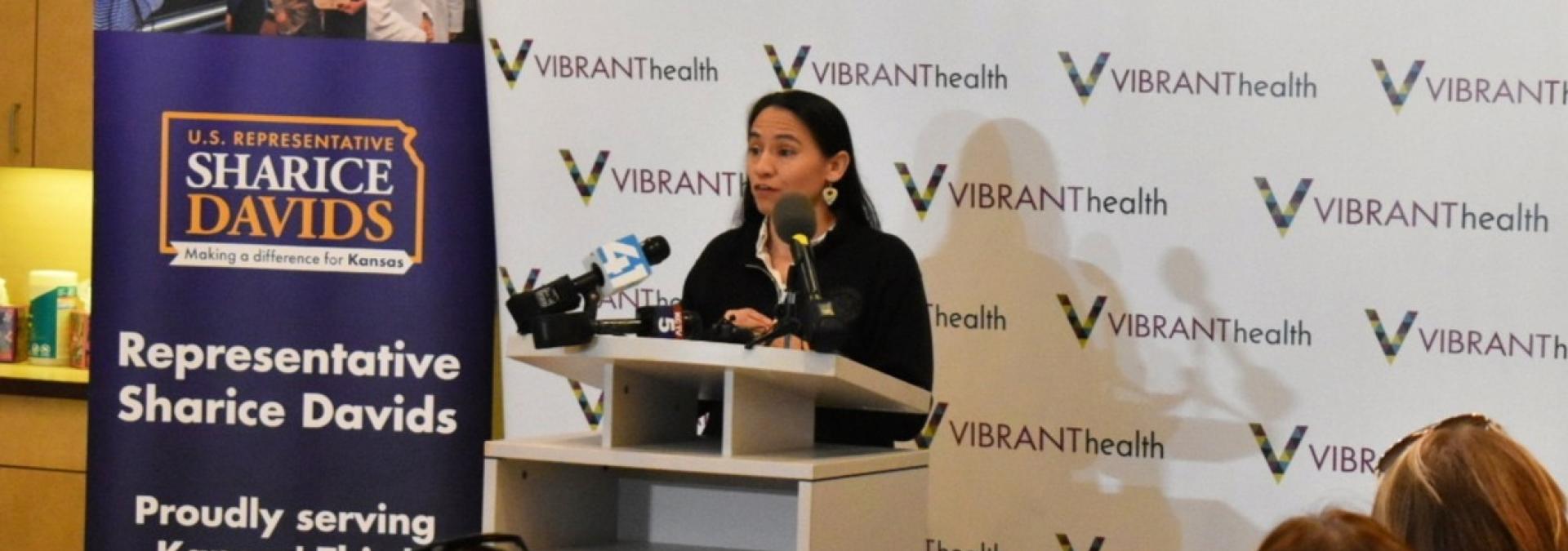Rep. Sharice Davids speaking at a podium at Vibrant Health in Kansas City, Kansas.