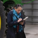 Rep. Sharice Davids stands in front of a tractor, writing in her notebook