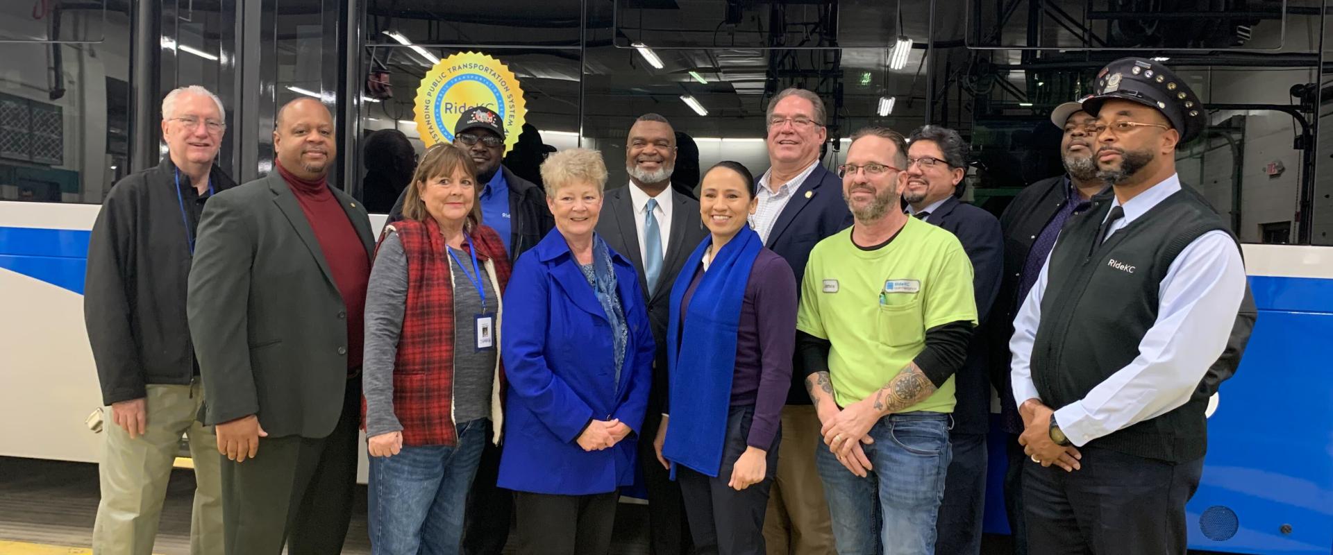 Rep Davids stands with a group of people in front of a city bus