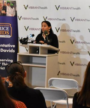 Rep. Sharice Davids speaking at a podium at Vibrant Health in Kansas City, Kansas.