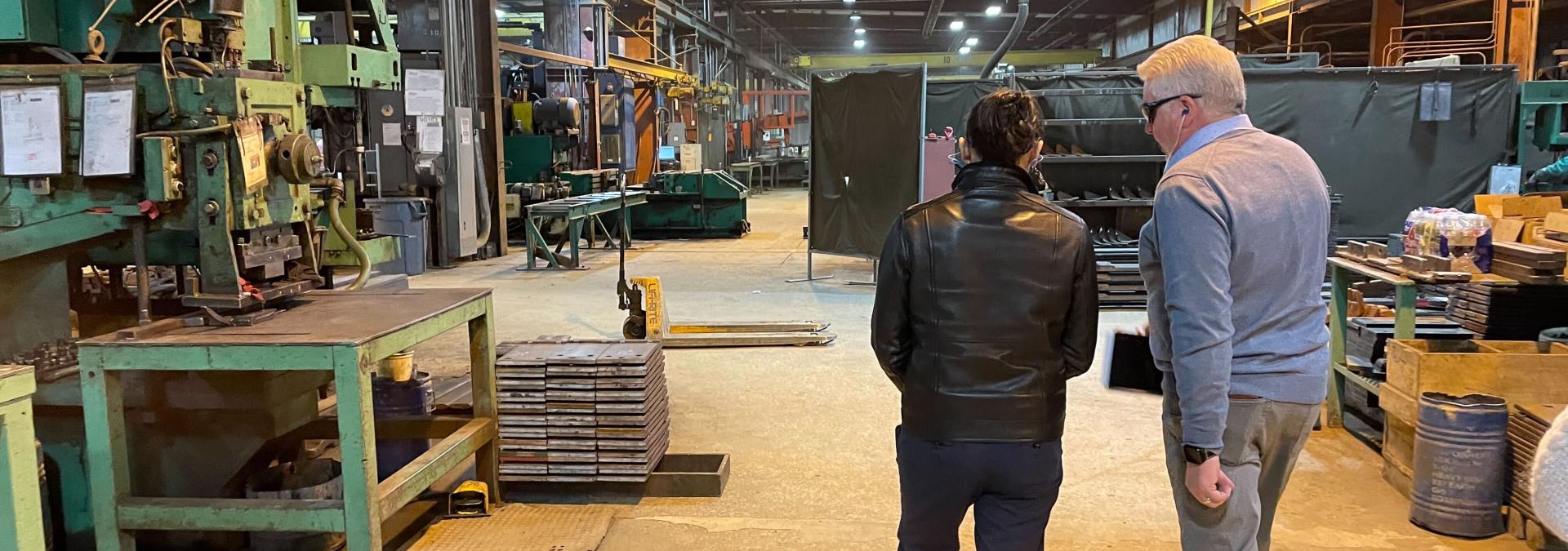 Two people walking into a manufacturing facility away from the camera